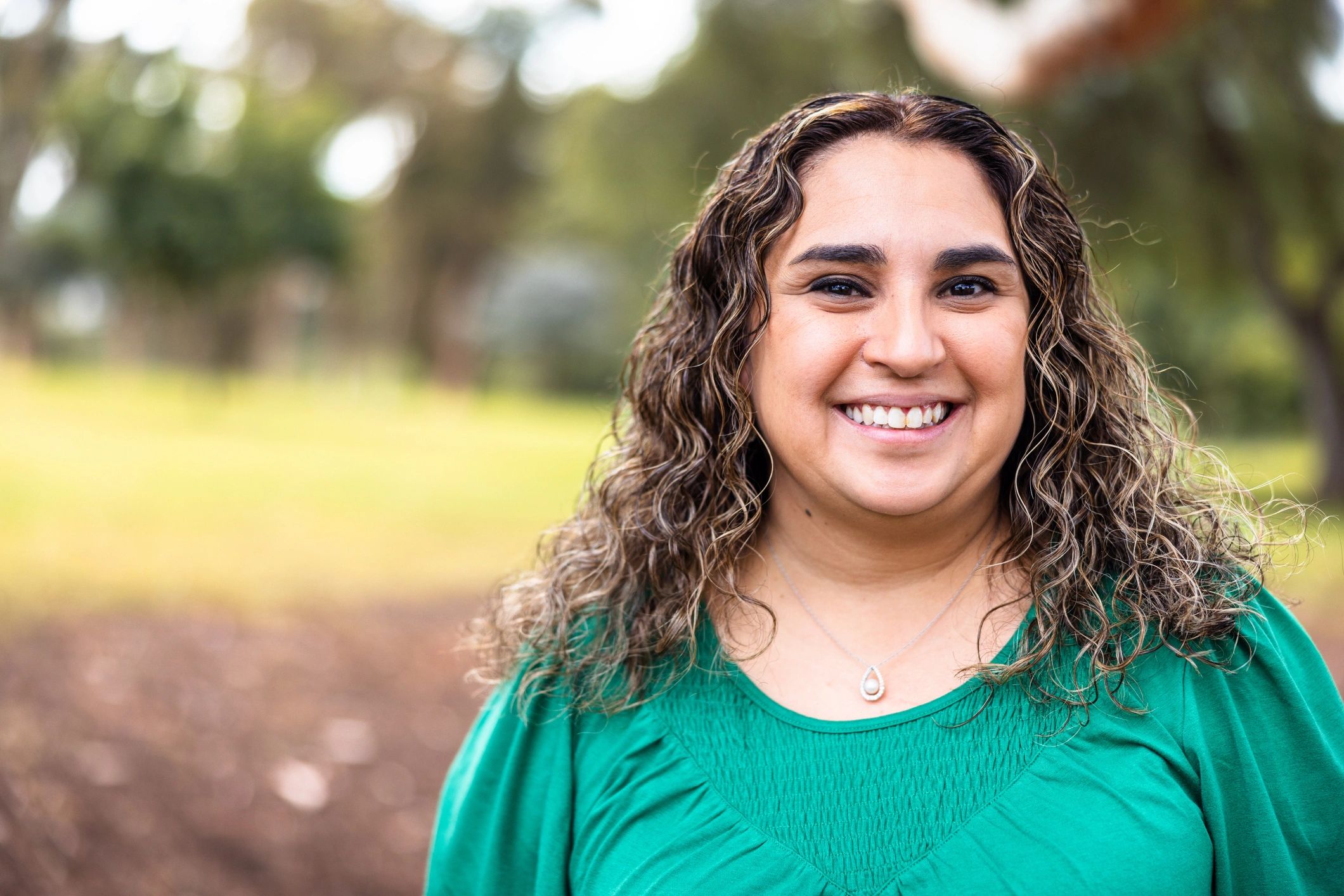 Smiling woman outdoors in a green top with curly hair.