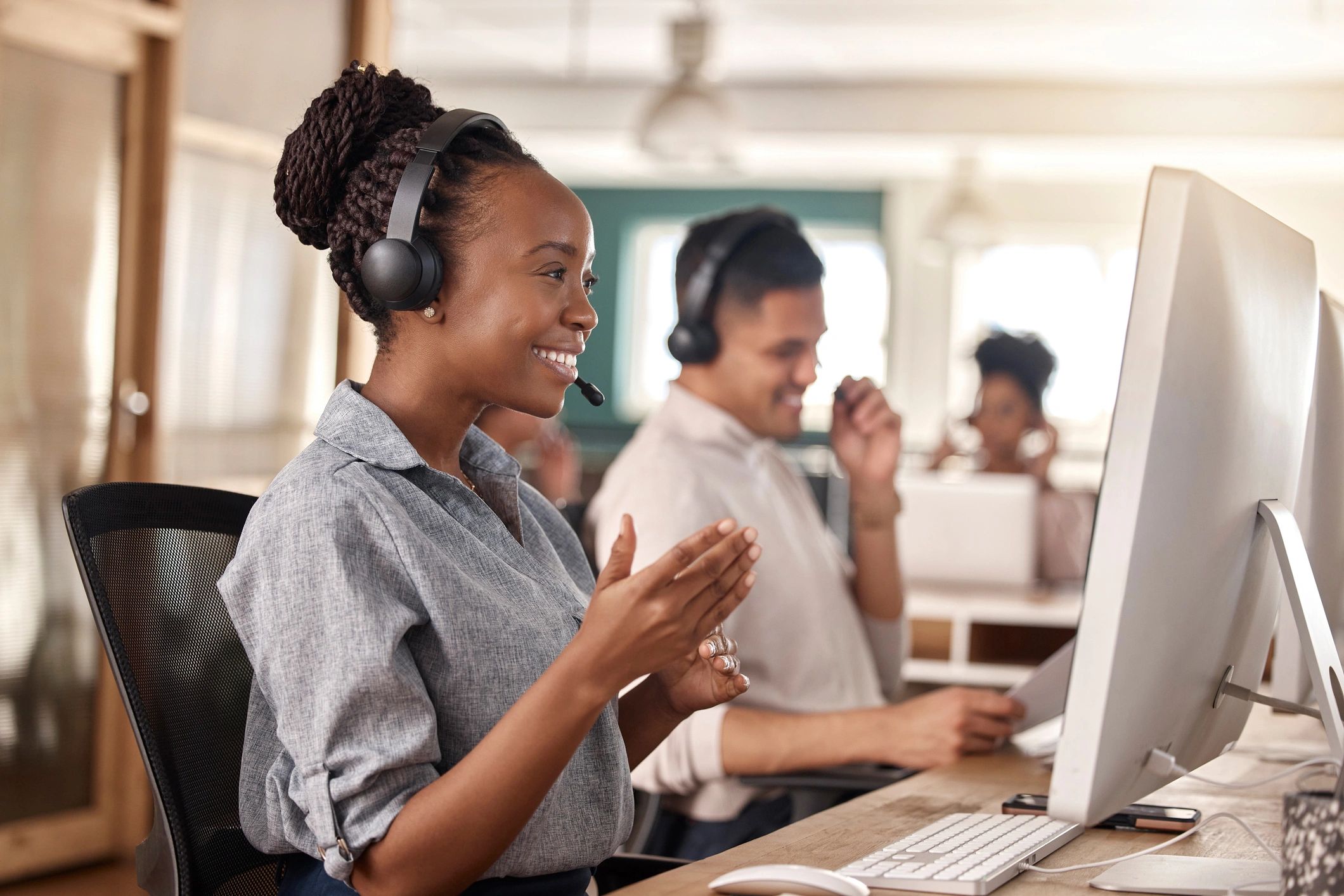 Two customer service representatives wearing headsets and smiling at their desks.