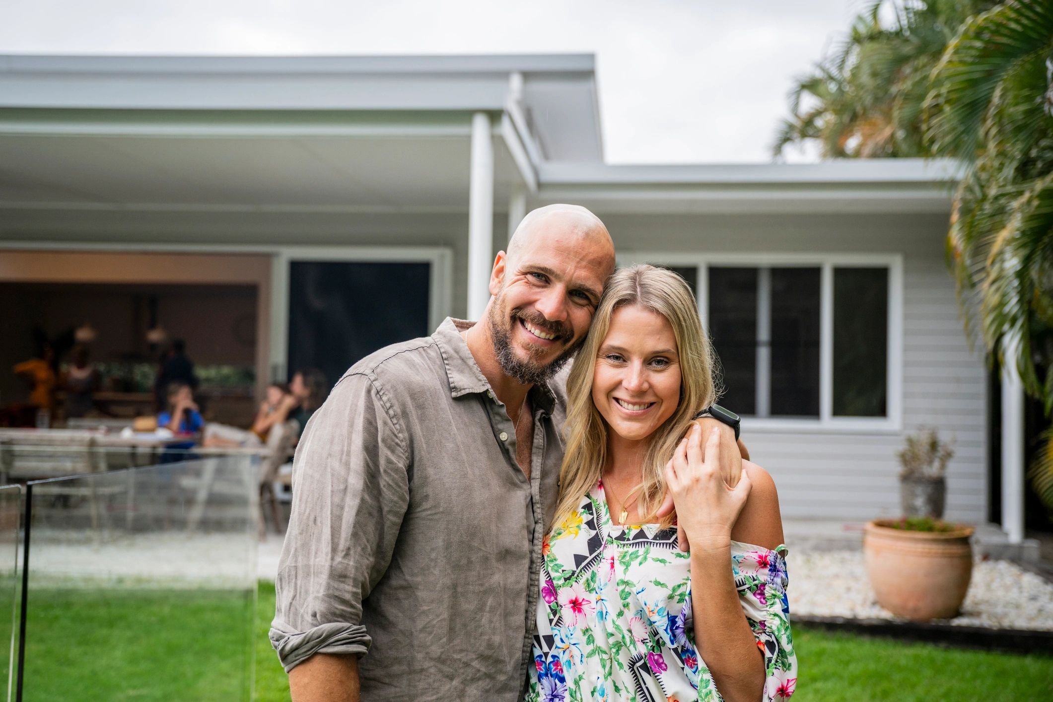 A happy couple posing outdoors with a house in the background.