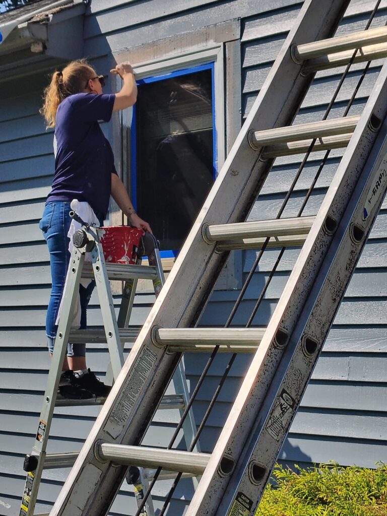 Two people installing or repairing a window on a house exterior.