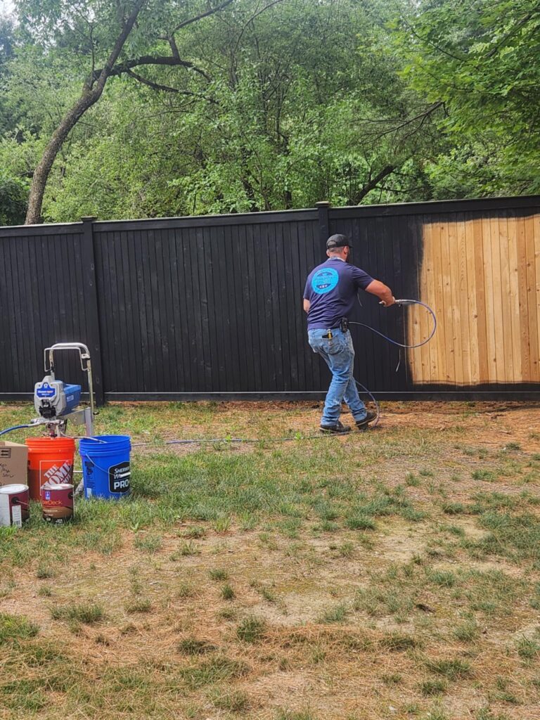 Man painting a fence with a roller outdoors.