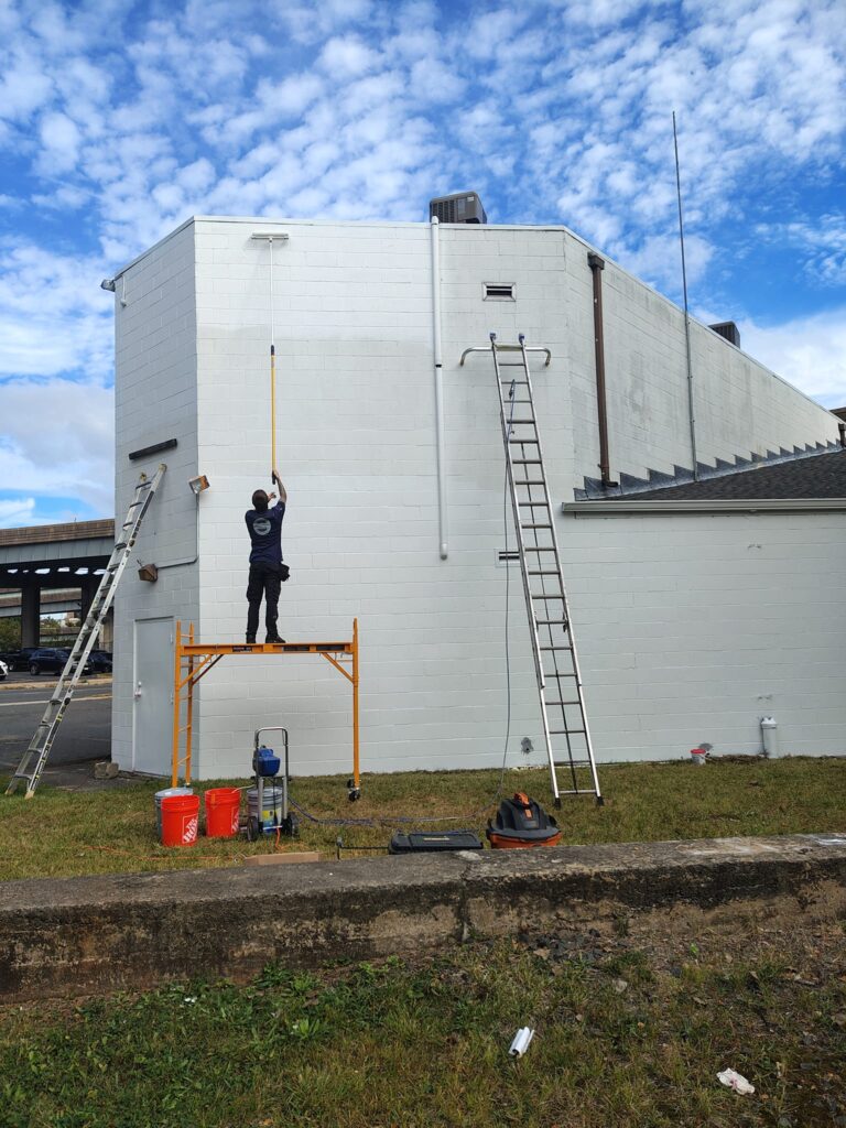Person on a table working on a ladder against a white building.