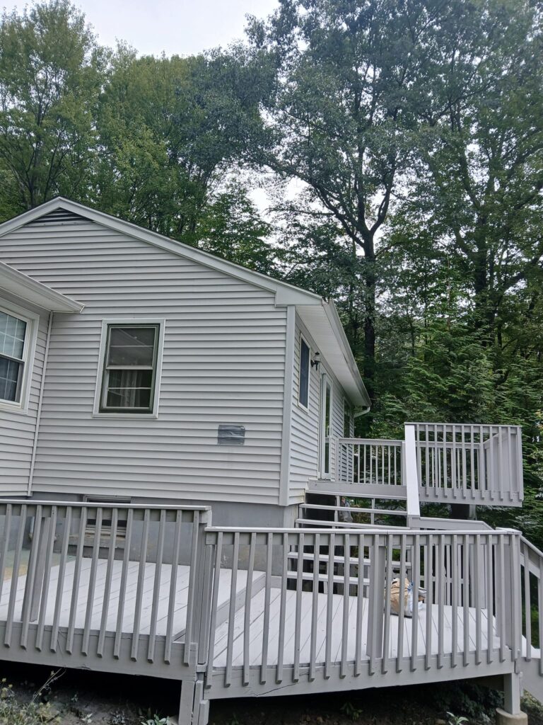 White wooden house with a small balcony surrounded by trees.