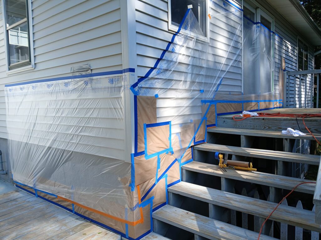 House exterior prepped with plastic sheeting and blue tape for painting.