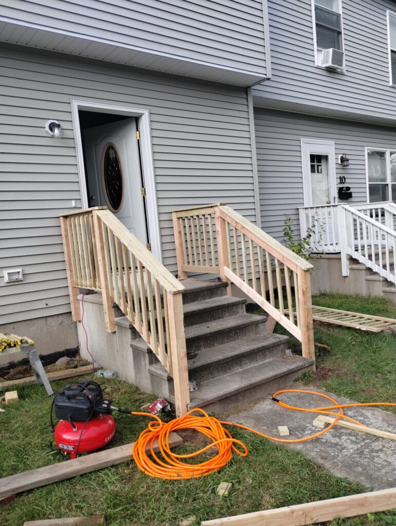 Newly built wooden porch steps with railing in front of a house.