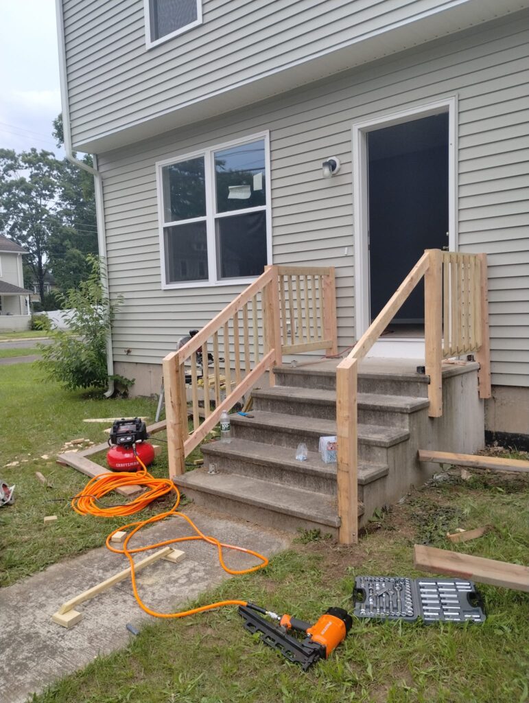 Newly built wooden stairs with railings leading to a house door.