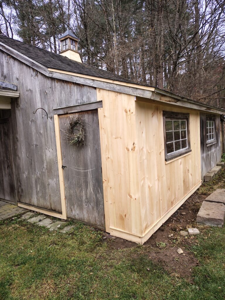 A small wooden shed with new light wood paneling and an older door.