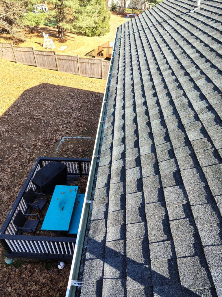 A view from a roof showing roof shingles and a backyard with a trampoline.