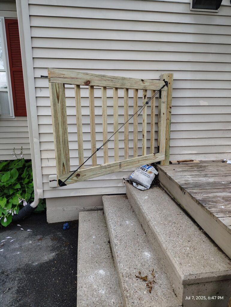A wooden gate blocks a set of stairs beside a house.