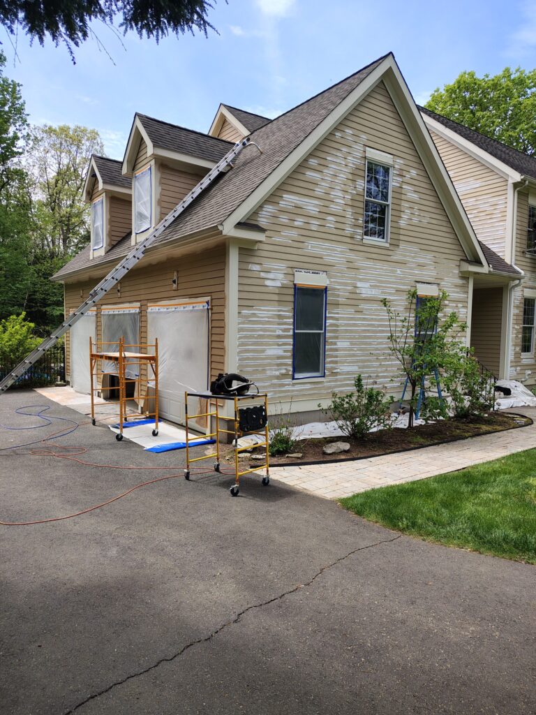 A two-story house with beige siding and a driveway under renovation.